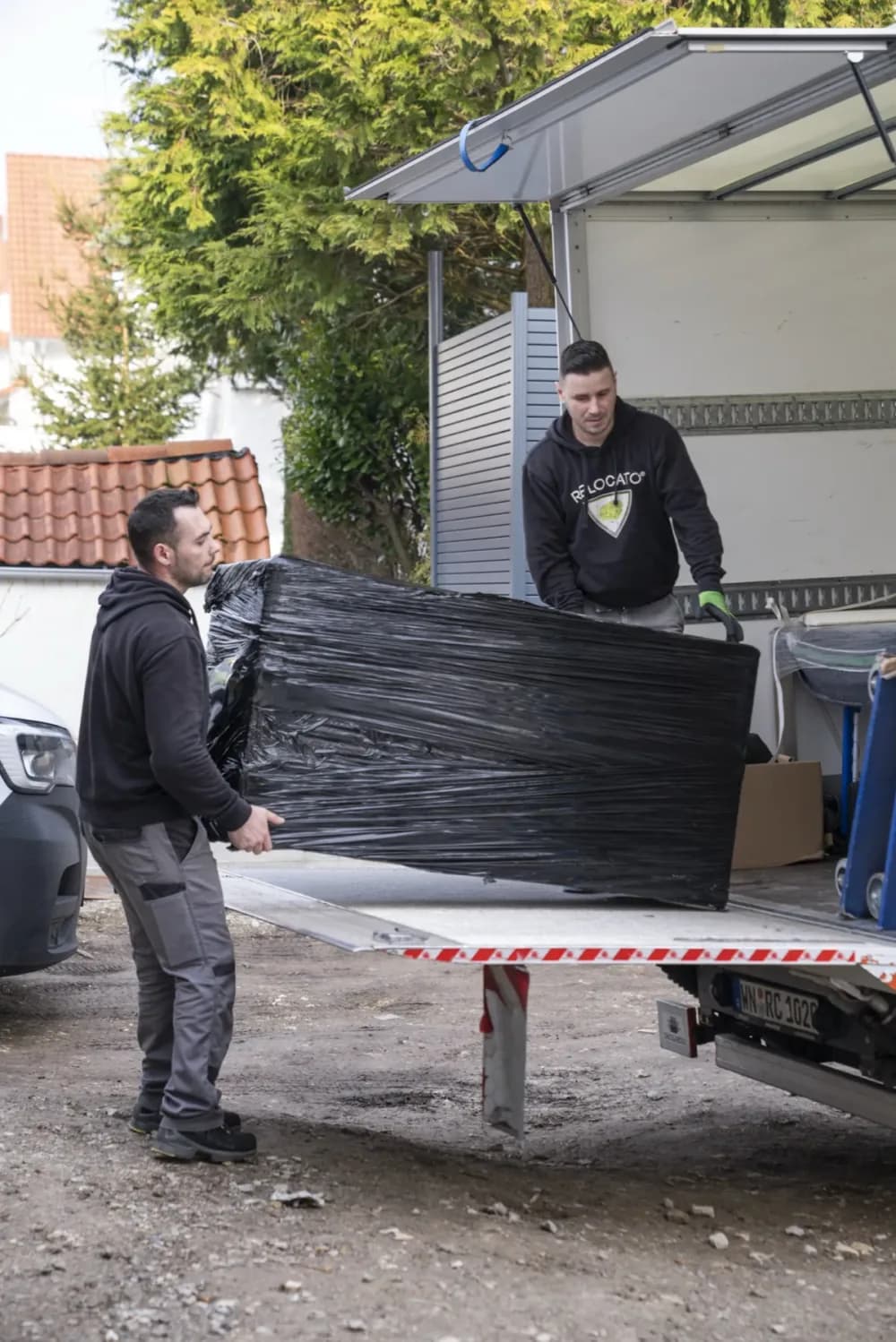 Zwei Relocato-Mitarbeiter verladen ein verpacktes Möbelstück in den LKW