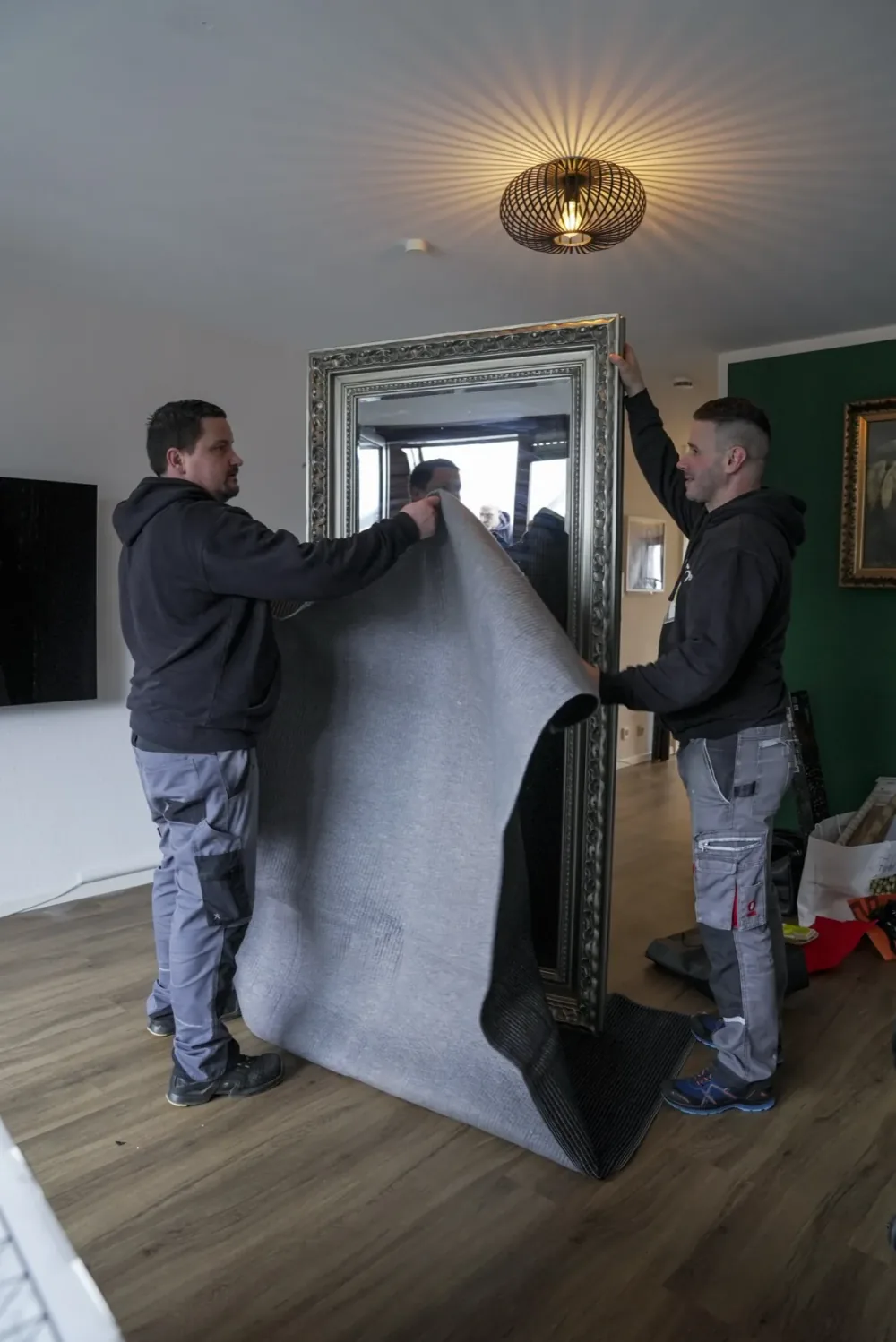 Zwei Relocato-Mitarbeiter tragen einen großen Standspiegel durch die Wohnung