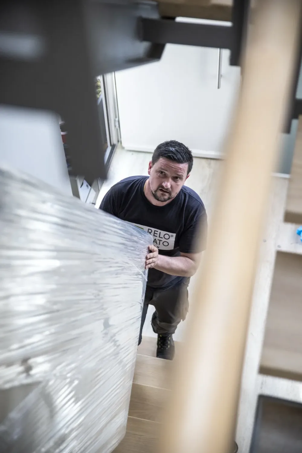 Relocato-Mitarbeiter trägt ein eingewickeltes Möbelstück die Treppe hinauf