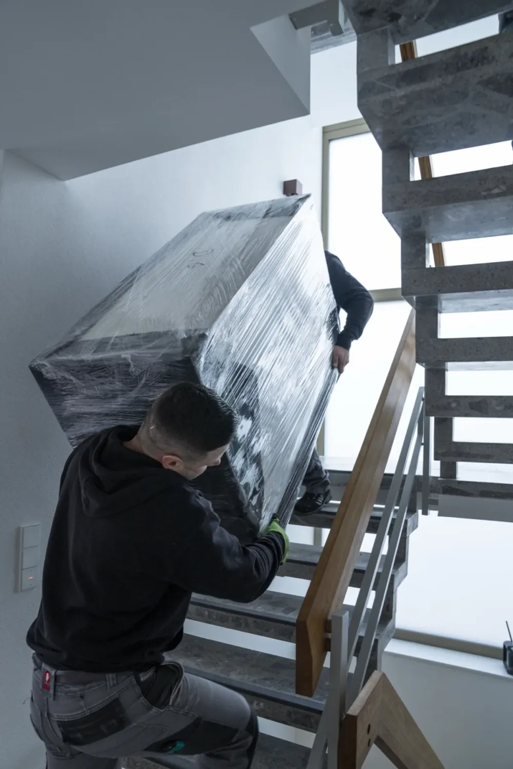 Relocato-Mitarbeiter tragen ein verpacktes Möbelstück die Treppe hinauf